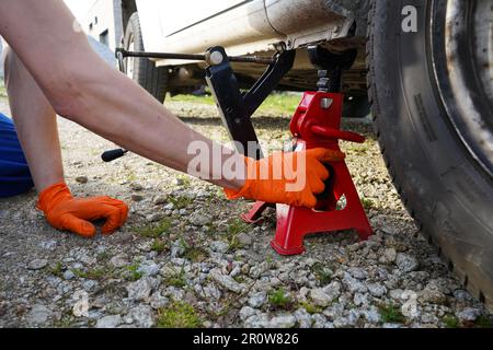 Das Fahrzeug wurde auf einem Wagenheber angehoben. Mechaniker hebt das Fahrzeug mit Wagenheber an. Reifenwechsel. Mechaniker wechselt Reifen im Auto. Stockfoto