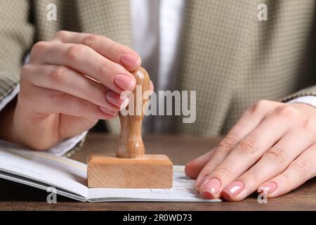 Ukraine, Lemberg - 6. September 2022: Frau stempelt Visumseite im Reisepass am Holztisch ab, Nahaufnahme Stockfoto