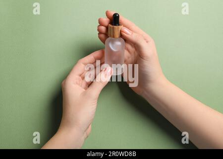 Eine Frau, die eine Flasche mit Serum auf olivem Hintergrund hält, Nahaufnahme Stockfoto