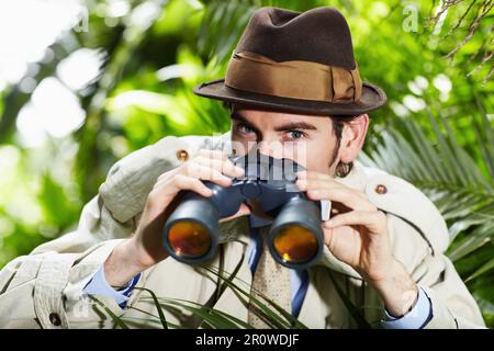Detective man, Suche und Porträt im Dschungel mit altmodischer Ausrüstung zur Ermittlung und Lösung. Draußen, Privatdetektiv und Spion mit Fernglas Stockfoto