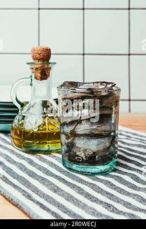 Vorderansicht des Haufen von gesalzenem Fisch im Glas auf dem Handtuch mit Flasche Öl- und Platten hinter Stockfoto