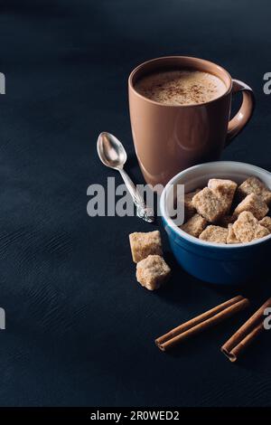 Tasse Kaffee, Schüssel mit braunem Zucker und Zimtstangen auf dunkler Oberfläche Stockfoto