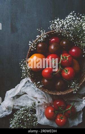 Frische rote Tomaten in Korbschale mit weißen Blumen auf Holzhintergrund Stockfoto