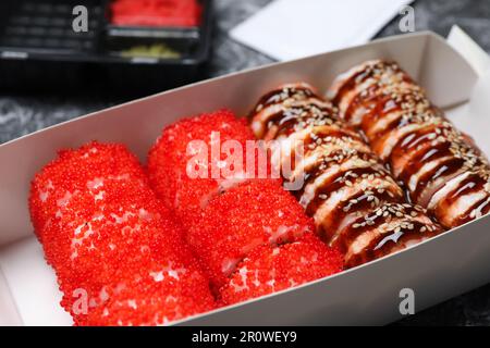 Verschiedene leckere Sushi-Brötchen in Pappkiste, Nahaufnahme. Lebensmittellieferung Stockfoto