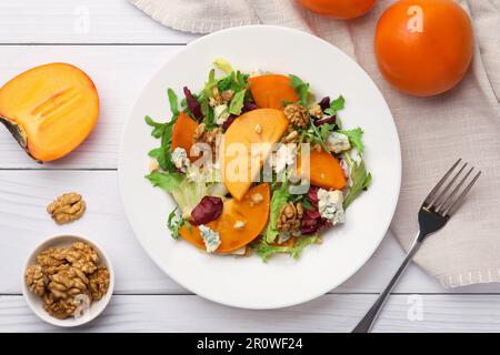 Köstlicher Persimonsalat und Gabel auf weißem Holztisch, flach liegend Stockfoto