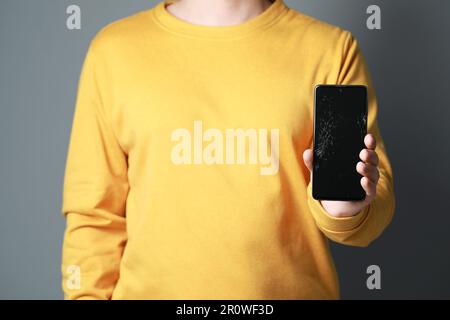 Mann zeigt ein beschädigtes Smartphone auf hellgrauem Hintergrund, Nahaufnahme. Gerät wird repariert Stockfoto
