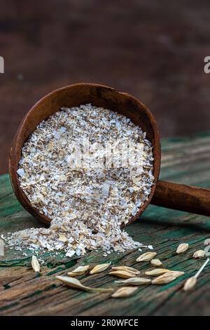 Nahaufnahme eines Holzlöffels voller Haferflocken neben Haferkörnern Stockfoto