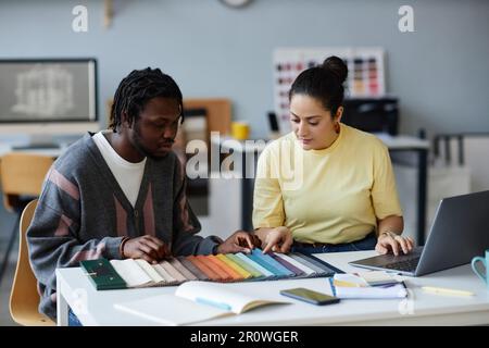 Junge Kollegen diskutieren Farben auf Palette, während sie im Team am Tisch im Büro stehen Stockfoto