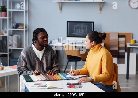 Zwei Kollegen diskutieren über Design, während sie bei einer Besprechung im Büro am Tisch sitzen Stockfoto