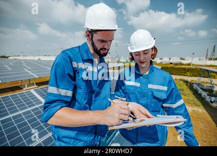 Solaringenieure untersuchen Schaltschrankarrays auf Bauernhöfen anhand von Bauplänen und Zeichnungen visuell, um sicherzustellen, dass Ausrichtung, Oberfläche, Sonnenlicht und zugänglich sind Stockfoto