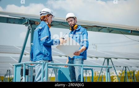 Solaringenieure untersuchen Schaltschrankarrays auf Bauernhöfen anhand von Bauplänen und Zeichnungen visuell, um sicherzustellen, dass Ausrichtung, Oberfläche, Sonnenlicht und zugänglich sind Stockfoto