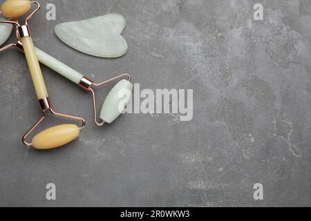 Gua-sha-Stein und verschiedene Gesichtsrollen auf grauem Tisch, flach liegend. Platz für Text Stockfoto