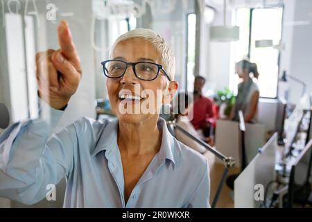 Reife Trainerin, die sich während der Workflow-Planungsstrategie für das Projekt Notizen macht Stockfoto