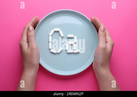 Frauen-Halteplatte mit Kalzium-Symbol aus weißen Pillen auf hellem rosa Hintergrund, Draufsicht Stockfoto