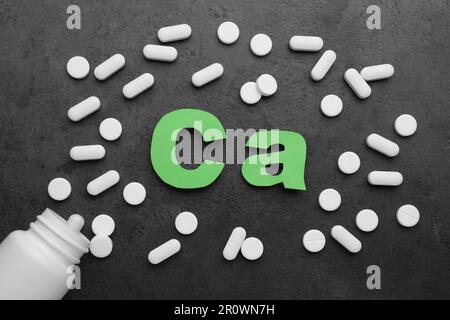 Papiersymbol Ca (Calcium), medizinische Flasche und Pillen auf schwarzem Hintergrund, flach liegend Stockfoto