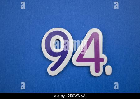 Die Nummer 94, auf blauem Hintergrund, von oben fotografiert, blau und lila. Stockfoto