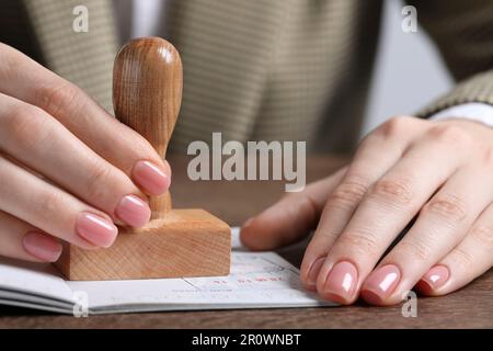 Ukraine, Lemberg - 6. September 2022: Frau stempelt Visumseite im Reisepass am Holztisch ab, Nahaufnahme Stockfoto