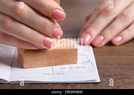 Ukraine, Lemberg - 6. September 2022: Frau stempelt Visumseite im Reisepass am Holztisch ab, Nahaufnahme Stockfoto