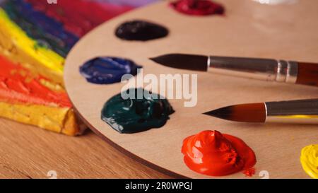Künstlerpalette mit Mustern von bunten Farben und Pinseln auf Holztisch, Nahaufnahme Stockfoto