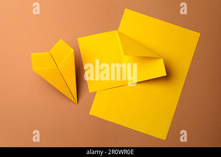 Handgefertigtes gelbes Flugzeug und Papierstücke auf braunem Hintergrund, flach liegend Stockfoto