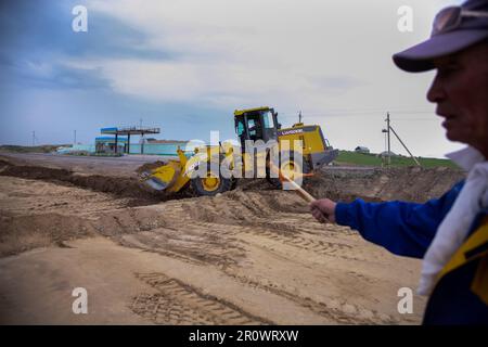 Südkasachstan - April 26 2012: Entwicklung der Straße zwischen Westeuropa und Westchina. Bodenarbeiten mit Bulldozer. Arbeiter mit Signalflagge rechts Stockfoto