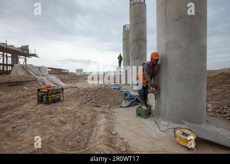 Südkasachstan - April 26 2012: Entwicklung der Straße zwischen Westeuropa und Westchina. Bau einer Brücke an der Straßenkreuzung. Baumeister bohrt Betonboden Stockfoto