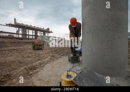 Südkasachstan - April 26 2012: Entwicklung der Straße zwischen Westeuropa und Westchina. Bau einer Brücke an der Straßenkreuzung. Baumeister bohrt Betonboden Stockfoto