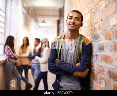 Freunde machen College-Spaß. Porträt eines hübschen jungen Studenten, der sich an einer Wand lehnte, mit seinen Freunden im Hintergrund. Stockfoto