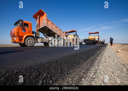 Provinz Kyzylorda, Kasachstan, 29. April 2012: Kipplaster entlädt heißen Asphalt. Bau einer neuen Autobahn zwischen Westeuropa und Westchina Stockfoto