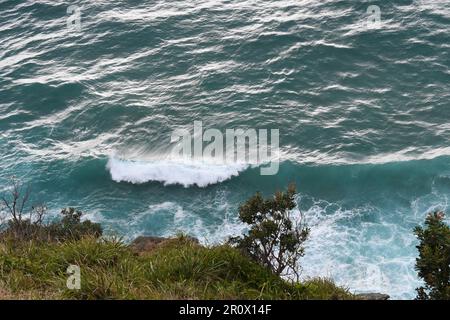 Aus der Vogelperspektive können Sie die wunderschönen Wellen des Ozeans sehen, die auf den felsigen Klippen der Byron Bay-Küste vom Leuchtturm aus stürzen Stockfoto