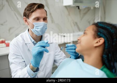 Porträt eines freundlichen männlichen Zahnarztes mit Maske und Handschuhen bei der Arbeit mit Teenagern in der Zahnklinik Stockfoto