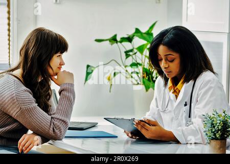 Junge Frau, die auf eine junge schwarze Ärztin hört Stockfoto