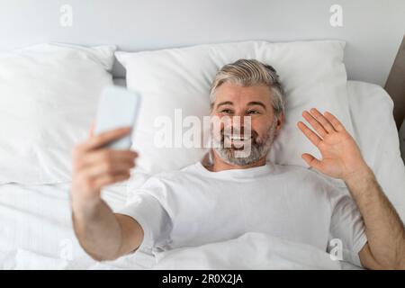 Draufsicht eines glücklichen Mannes, der im Bett telefoniert Stockfoto