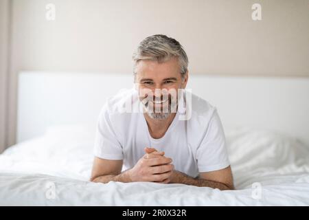 Porträt eines glücklichen Mannes mittleren Alters, der lächelnd im Bett liegt Stockfoto