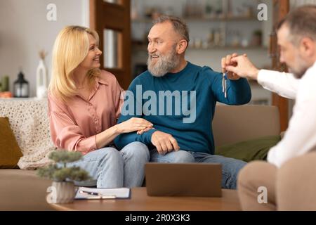 Ein Reifes Ehepaar, Das Hausschlüssel Von Einem Immobilienmakler Bekommt Stockfoto