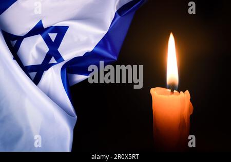 Holocaust-Gedenktag. Jom HaShoah. Leuchtende brennende Kerze und die offizielle Flagge Israels auf dunkelgrauem Hintergrund. Stockfoto