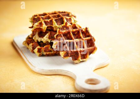 Hausgemachte kohlenhydratarme Zucchini-Waffeln auf weißem Holzbrett auf gelbem Hintergrund. Konzept der Keto-Diät. Stockfoto