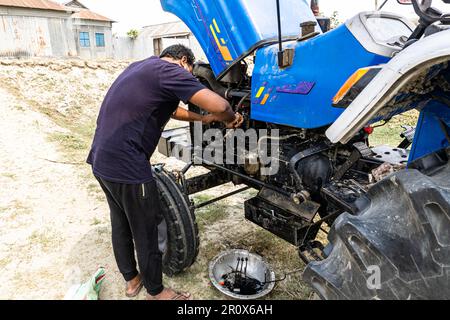 Bauernmechaniker, der den Motor eines blauen Traktors repariert. Maschinenwartung, mechanische Reparatur der Ölpumpe des Traktors und Prüfung des Ölstands im Freien Stockfoto