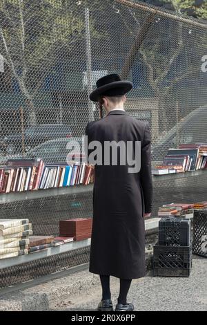 Ein anonymer junger jüdischer Mann, der ganz schwarz trägt, einschließlich hoher schwarzer Strümpfe, kaufte Bücher bei einem Pop-up-Verkauf im Freien. In Brooklyn, New York. Stockfoto