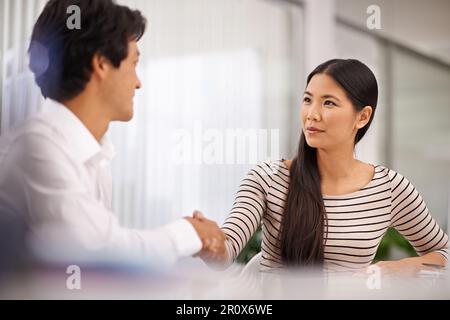 Ich denke, das lief wirklich gut. Zwei Geschäftsleute schütteln sich die Hand, während sie in einem Büro sitzen. Stockfoto