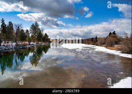 Ein gefrorener Wintersee, umgeben von Laub unter dem wolkigen blauen Himmel in Bend Stockfoto