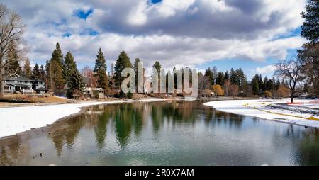 Ein gefrorener Wintersee, umgeben von Laub unter dem wolkigen blauen Himmel in Bend Stockfoto