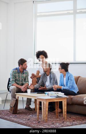 Junge Köpfe bei der Arbeit im Büro. Eine vielfältige Gruppe junger Designer, die sich unterhalten, während sie auf dem Sofa in einem Büro sitzen. Stockfoto