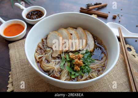 Entennudelsuppe: Geschmorte Entennudeln in einer weißen Schüssel mit Holztisch aus nächster Nähe, asiatische Gerichte Stockfoto