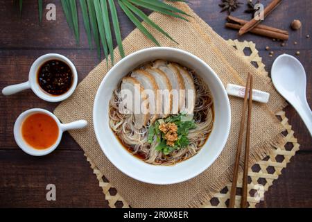 Entennudelsuppe: Geschmorte Entennudeln in einer weißen Schüssel mit Holztisch von oben, asiatische Gerichte Stockfoto