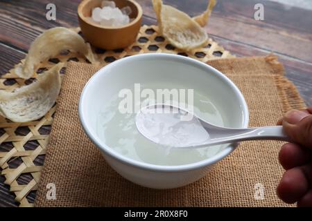 Essbare Vogelnest-Suppe mit Steinzucker in einer weißen Schüssel bei Nahaufnahme auf dem Holztisch Stockfoto