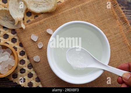 Essbare Vogelnest-Suppe mit Steinzucker in einer weißen Schüssel bei Nahaufnahme auf dem Holztisch Stockfoto