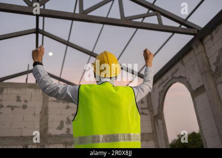 Asiatischer Ingenieur in Uniform und Helm auf der Baustelle, glücklich und lächelnd für den Erfolg. Erfolgreiches Projekt und Happiness Expression After Work Konzept Stockfoto