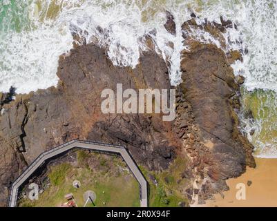Aus der Vogelperspektive sehen Sie die Wellen, die an einer felsigen Küste unter einer Promenade bei South West Rocks in New South Wales, Australien, anschwellen Stockfoto