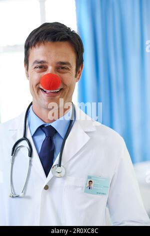 Lachen ist die beste Medizin. Porträt eines gutaussehenden, lächelnden jungen Arztes mit roter Clownnnase. Stockfoto